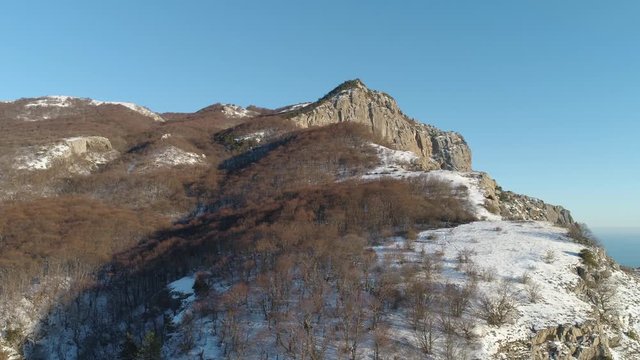 Aerial view of sunny Alp mountains in winter covered by snow and bald trees on blue sky background. Shot. Flying over steep cliffs on a sunny day.