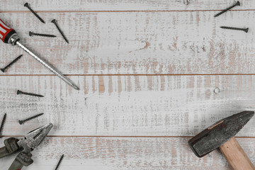 A hammer, screwdriver, pliers and screws lie on a wooden table