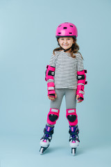 Smiling little girl in roller skates with pink protective gear over blue