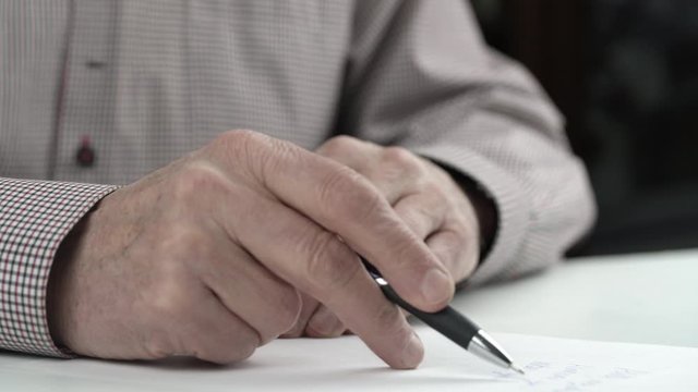 wise old man wearing checkered shirt rereads letter to family on white paper sheet and signs at end extreme close view