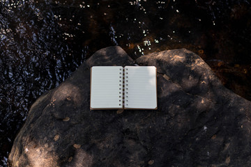 Book and glasses on a rock in the stream in the middle of nature.