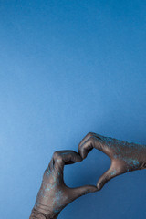 The heart, figure built from the hands in balck rubber medical gloves with glitter on a blue background. Tattoo master, cosmetology, beauty industry concept of love client, banner, copy space
