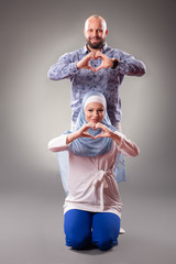 Fototapeta na wymiar Happy couple in love posing on the gray background. Heart shape with hands
