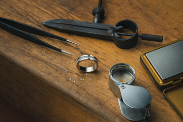Jewelry craftsmanship. Jeweller at work. The jeweller engraver tools and golden ring, diamonds on...