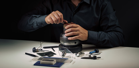 Obraz premium Jewelry craftsmanship, engraving. Jeweller engraver hands at work. Professional engraver tools for jewelleries manufacturing on white desk. Craftsman, engraver, goldsmith workplace 