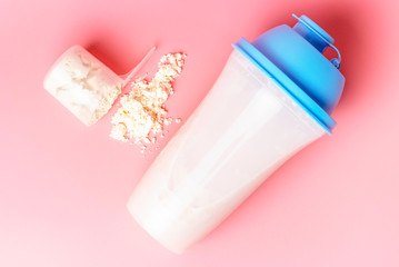 Cocktail shaker and measuring spoon with protein on pink background.