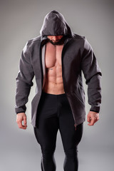 Fototapeta na wymiar Sexy muscular bodybuider posing with sweatshirt and hood on the gray background