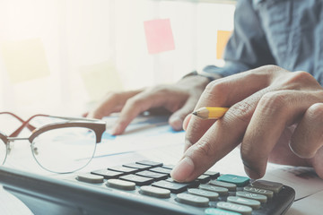 Close up Businessman using calculator and laptop for do math finance on wooden desk in office and business working background, tax, accounting, statistics and analytic research concept