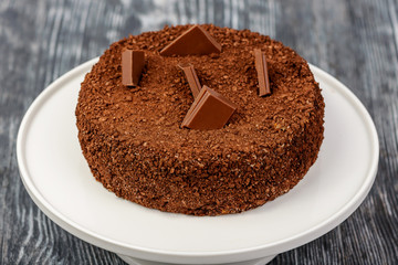 Chocolate biscuit cake with pieces of dark chocolate and a sprinkle of cocoa on a white stand