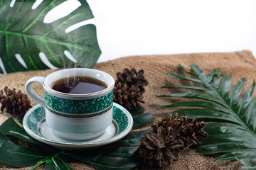 Cup of black tea with smoke on burlap with leaves 