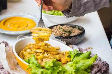 Homemade golden salty french fried potato with green salad leaves. Roasted or grilled spicy potato sticks in woman hands.