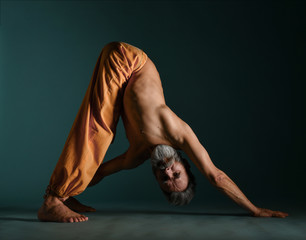 Old man with grey beard doing yoga, pilates, fitness training, stretching exercise, asana or...