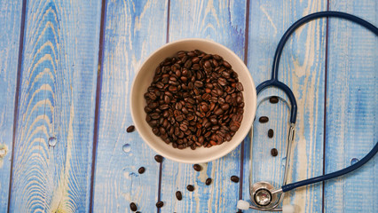 Des grains de café dans un bol avec un stéthoscope sur une table en bois rustique de couleur bleu...