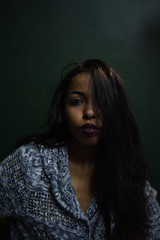 young African woman posing at studio, face with hand portrait over dark background	