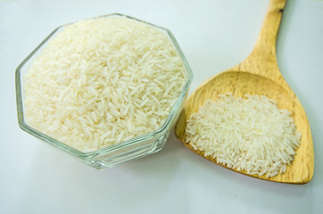 Milled rice in glass cup and wooden spoon for cooking