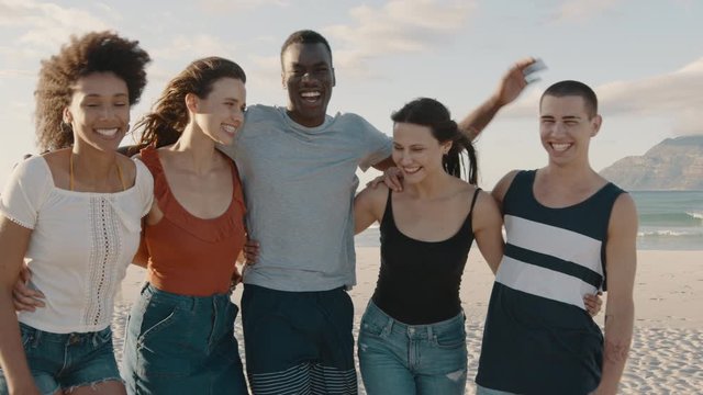 Group of men and women standing together on the beach and smiling. Multi-ethnic group of friends looking t camera and laughing.