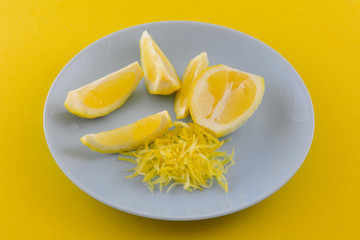 Lemon half, lemon wedges and lemon zest on blue plate on yellow background