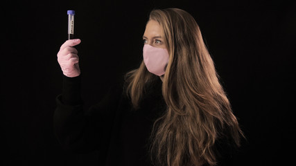 Obraz premium Girl in a pink mask holds a test tube with blood and the inscription covid-19 and twists the mask. Isolated on black background. Health care and medical concept. Coronavirus Epidemic