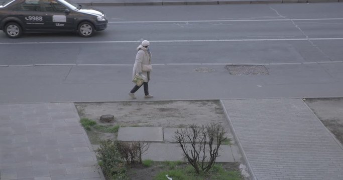 A Poorness Woman Passing Along the Street Covering Her Face With Her Hand, in a Medical Mask During Quarantine. Сars are Driving in the Background.