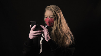 Girl with a white ribbon and the inscription covid 19 in red mask takes selfie on smartphone. Isolated on black background. Health care and medical concept. Coronavirus Epidemic
