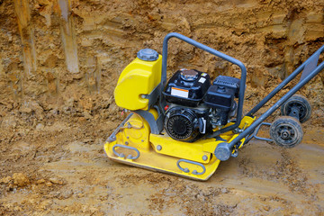 Tamping machine preparation of the ground by vibratory plate compactor in construction rammer in foundation pit for construction of building.