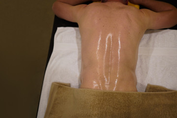 a back of male laying down on the massage table with his body applied oil look shinny
