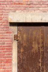 Old weathered rusty factory gate and the dated brown brick wall in the sunlight
