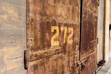 Old weathered rusty factory gate with number in the sunlight