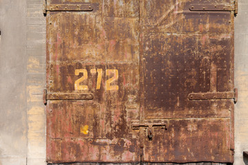 Old weathered rusty factory gate with number and the dated brown brick wall in the sunlight