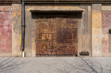 Old weathered rusty factory gate and the dated brown brick wall in the sunlight