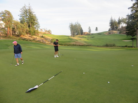  A father and son on a putting green playing golf surrounded by beautiful scenery outside of Victoria, British Columbia, Canada.