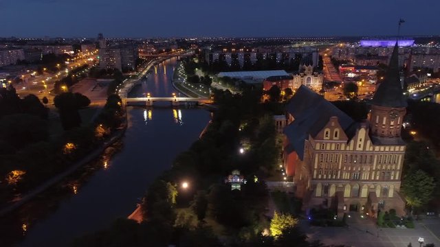 Aerial sideways Kaliningrad night city landscape general plan. Evening illumination. Historic city center main attractions. Gothic cathedral, fishing village, river, bridges. Unique light reflection