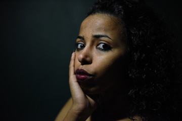 young naked African woman posing at studio, face with hand portrait over dark background