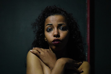 young naked African woman posing at studio, face with hand portrait over dark background	