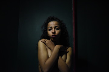 young naked African woman posing at studio, face with hand portrait over dark background	