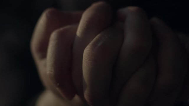 Hands clasped and squeezing tightly together in dark room, close-up