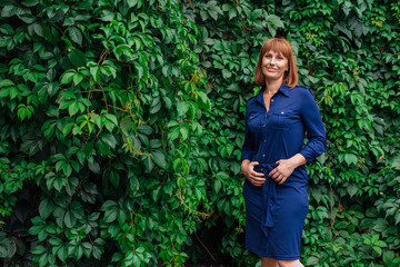 Portrait of a beautiful middle aged woman, standing next to the wall of wild grape leaves.