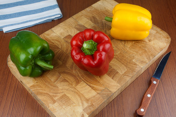 Three chili bell pepper on a wooden cutting board with knife on the table.