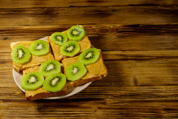 Tasty sandwiches with peanut butter and kiwi fruits on wooden table