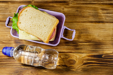 Lunch box with sandwiches and bottle of water on a wooden table. Top view