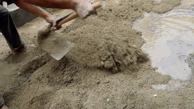 Indian labour mixing cement and water manually on floor using a shovel. Stcok footage.