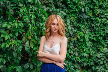 Portrait of a young beautiful woman, standing next to the wall of wild grape leaves.