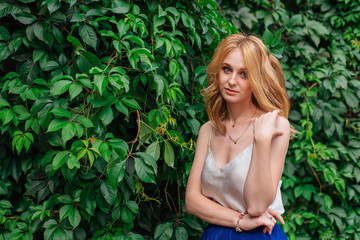 Portrait of a young beautiful woman, standing next to the wall of wild grape leaves.