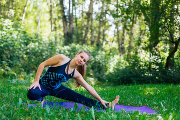 Naklejka na ściany i meble Young woman doing yoga exercises in summer city park.