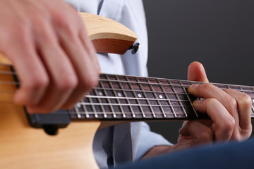 Male arms holding and playing classic shape wooden electric guitar closeup. Six stringed learning...