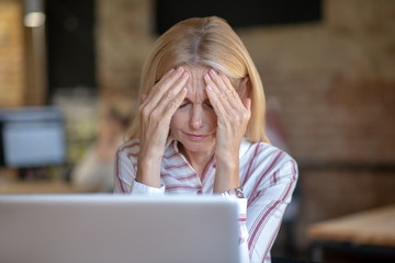 Blonde woman suffering from headache, holding her forehead