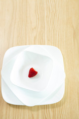 테이블 위의 흰 접시에 빨간 딸기 한 개