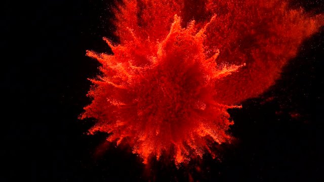 In real slow motion footage against a black background, a haphazard pile of bright red powder explodes like a firework in all four directions. Top shot.