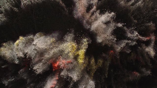 In real slow motion footage, a sea of dark grey powder bursts in all directions to reveal sparkling veins of bright red and gold. Top shot