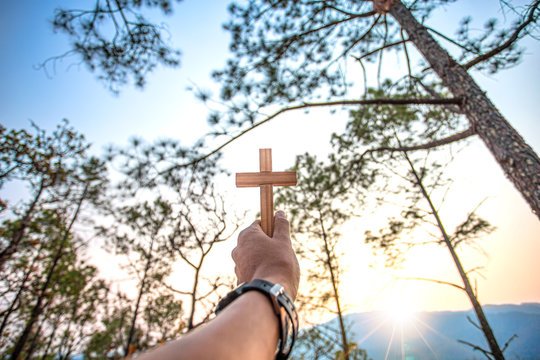 Human hand holding and lift christian Cross with sunlight  background, Christian concept.